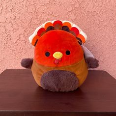 a stuffed turkey sitting on top of a wooden table next to a pink wall and a brown shelf