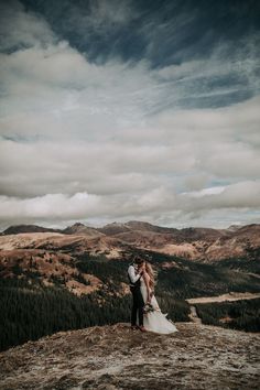 a bride and groom standing on top of a mountain