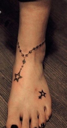 a woman's foot with a chain and stars tattoo on the bottom of it