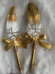 two golden feathers with white and gold accents on them, tied together by ribbons in the shape of arrows