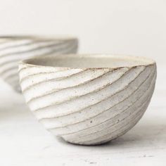 two white bowls sitting on top of a table next to each other with wavy designs