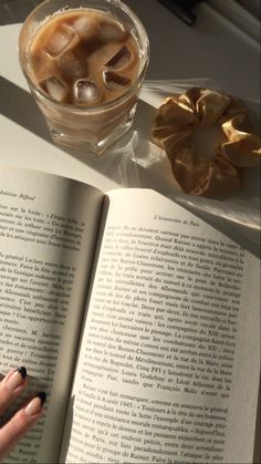 an open book sitting on top of a table next to a glass filled with liquid