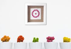 four white vases with colorful flowers in them next to a framed picture on the wall