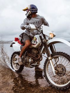 a man riding on the back of a white dirt bike in the mud near water