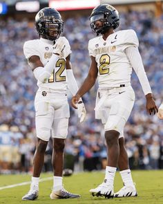 two football players standing next to each other on a field with fans in the background