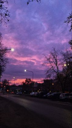 the sky is purple and there are cars parked on the side of the road