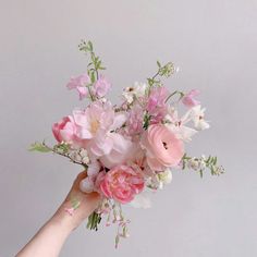 a person's hand holding a bouquet of pink and white flowers on a gray background