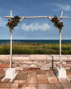 an outdoor ceremony setup with flowers and greenery on the top, in front of the ocean