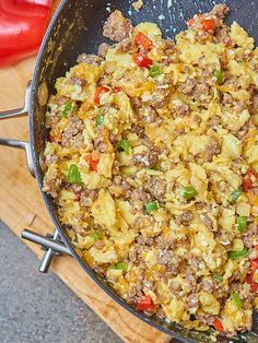 a skillet filled with eggs and meat on top of a wooden cutting board next to peppers