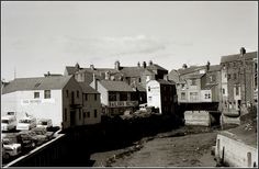 an old black and white photo of some buildings in the distance with cars parked on the street