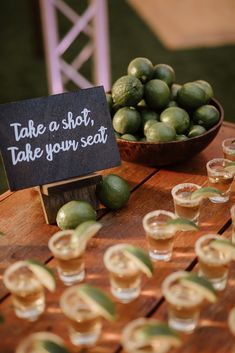 a table topped with lots of glasses filled with green fruits and veggies next to a sign that says take a shot, take your seat