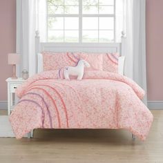 a pink and white bed with a unicorn on the comforter in front of a window