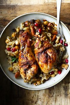 two pieces of chicken on top of rice with pomegranates and nuts