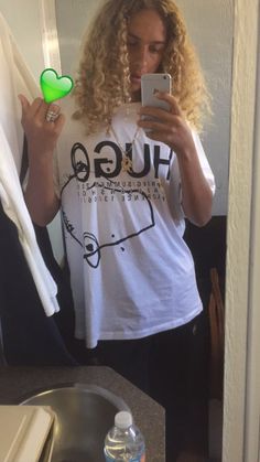 a woman taking a selfie in the mirror with her cell phone and wearing a t - shirt that says hug