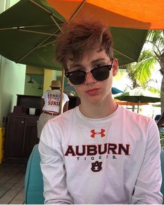 a young man wearing sunglasses sitting under an umbrella