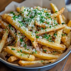 french fries with parmesan cheese and herbs in a bowl on a wooden table