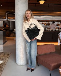 a woman standing next to a tall pillar holding a black handbag in her right hand