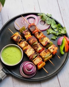 a plate filled with skewers of food next to a bowl of dipping sauce