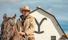 a man riding on the back of a brown horse next to a white building with a y painted on it