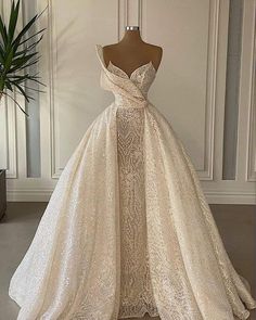 a wedding dress on display in front of a white wall with a potted plant