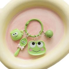 two keychains with faces on them are sitting in a bowl, one is green and the other is pink