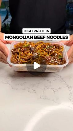 someone holding up a container of noodles with beef and vegetables in it on a counter top