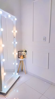 a lighted mirror sitting on top of a white tiled floor next to a table with flowers