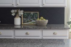 a bowl of fruit sitting on top of a counter next to a vase with flowers