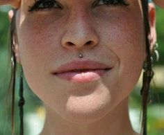 a close up of a woman with freckles on her head and nose piercings