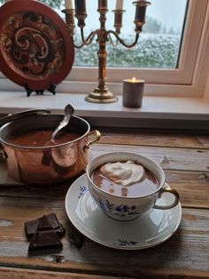 a cup of hot chocolate with marshmallows in front of a candle and window