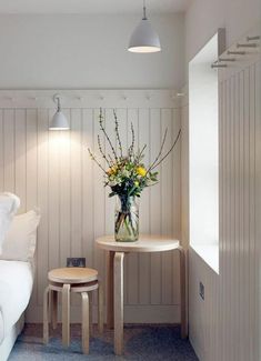 a vase with flowers sitting on top of a small table next to a white bed