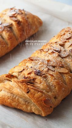 two croissants with almonds on them sitting on top of a piece of parchment paper