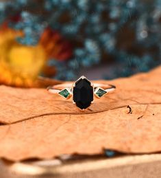 a black diamond ring sitting on top of a brown leaf next to a yellow flower