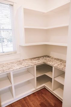 an empty kitchen with white cabinets and marble counter tops in the corner, next to a window