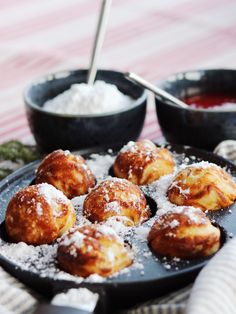 powdered sugar covered pastries on a black plate with bowls of sauces in the background