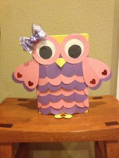 a paper owl sitting on top of a wooden table next to a brown chair with a purple bow