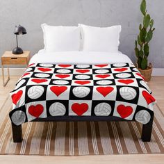 a bed covered in a blanket with hearts and volleyballs on the cover, next to a potted plant