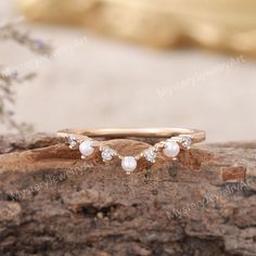 two gold rings with pearls and diamonds on top of a tree stump in front of some flowers