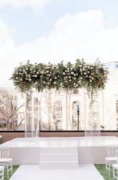 an outdoor ceremony setup with white chairs and flowers on the back drop off table for seating