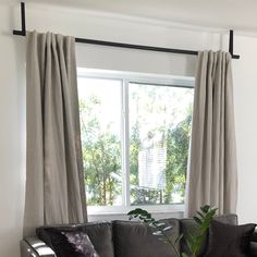 a living room filled with furniture and a large window covered in draping next to a potted plant