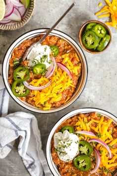 two bowls filled with chili and cheese on top of a table