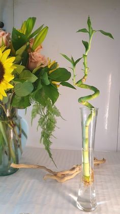 two vases with flowers in them sitting on a table next to another vase filled with water and sunflowers