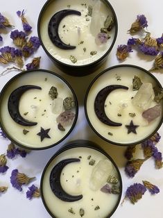 four black bowls filled with white liquid and some purple flowers on the table next to them