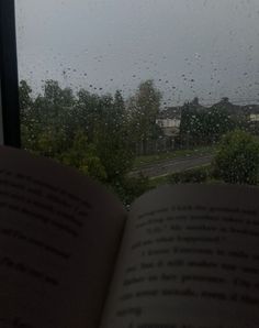 an open book sitting on top of a window sill next to a rain soaked window