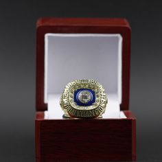 a gold and blue ring sitting in a red box on top of a wooden stand