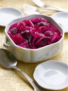 a white bowl filled with red onions next to two spoons