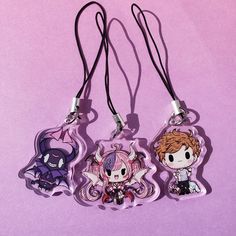 three keychains with anime characters on them sitting on a purple surface next to each other