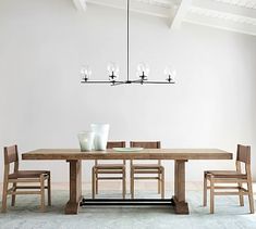 a dining room table and chairs in front of a white wall with a chandelier