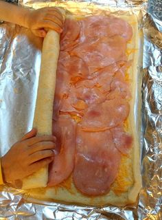 a person holding a long piece of bread with bacon on it in front of a sheet of aluminum foil