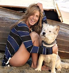 a woman kneeling down next to a dog on the beach